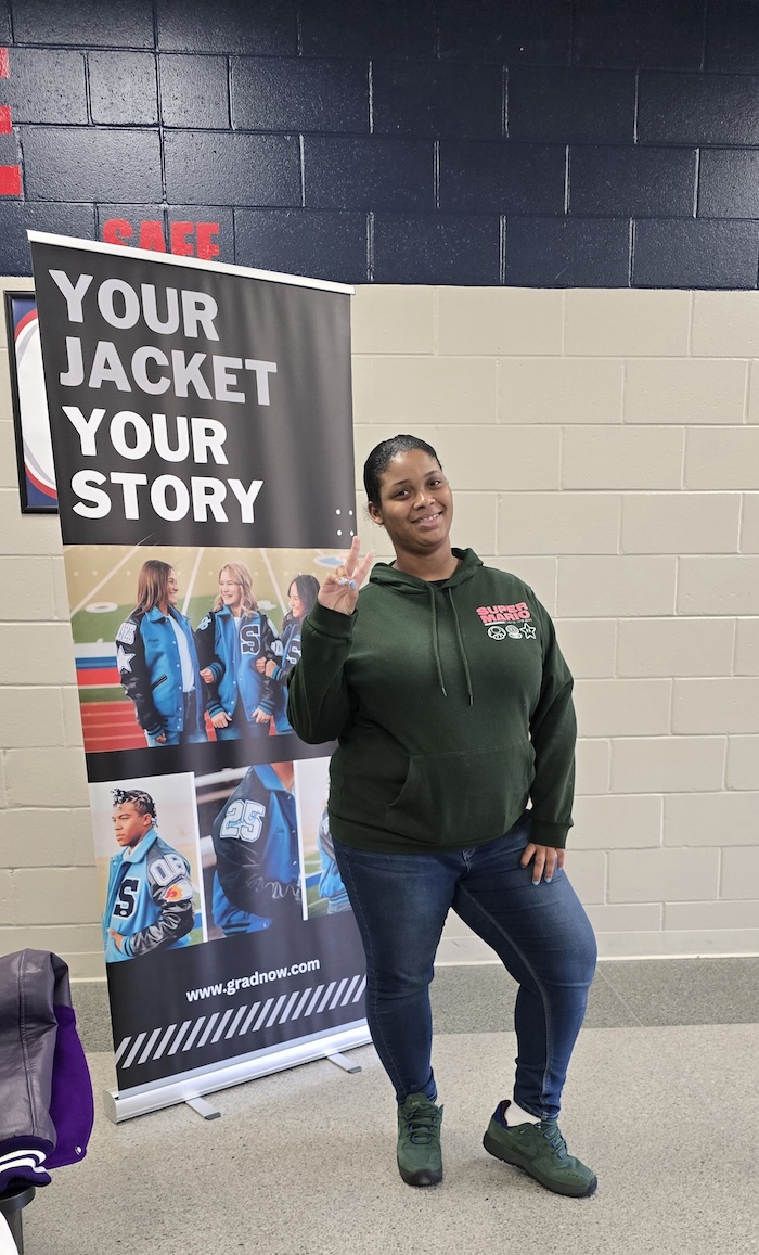 Zoe in front of "Your Jacket Your Story" gradnow.com sign